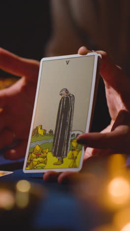 Vertical-Video-Close-Up-Of-Woman-Giving-Tarot-Card-Reading-On-Candlelit-Table-Holding-Death-Card-2